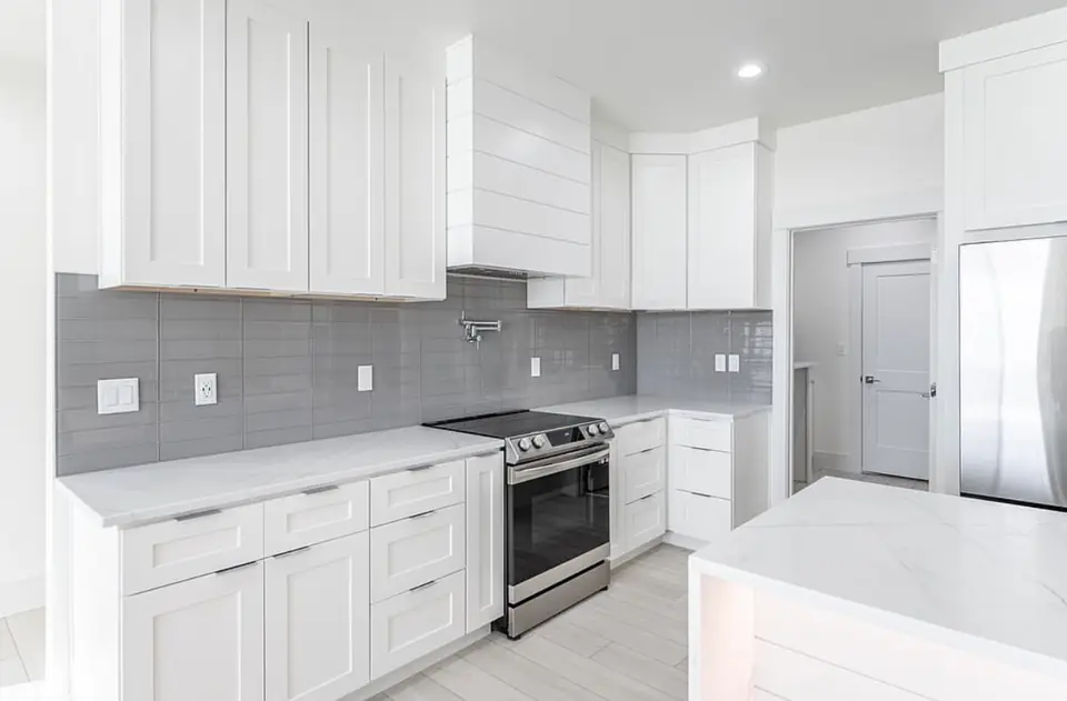 White shaker kitchen cabinets with gray tile backsplash, pot filler, stainless range and quartz countertops